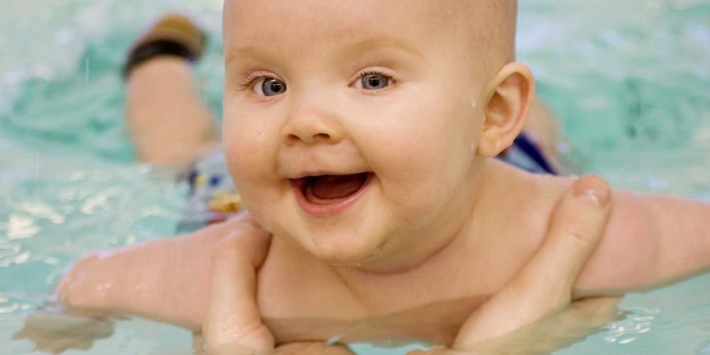Bebis som badar i bassäng med en vuxen